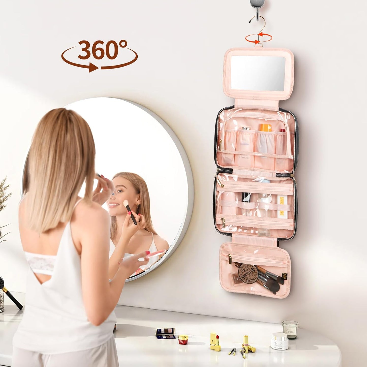 Woman applying makeup in front of a round mirror with a pink cosmetic bag hanging on the wall.